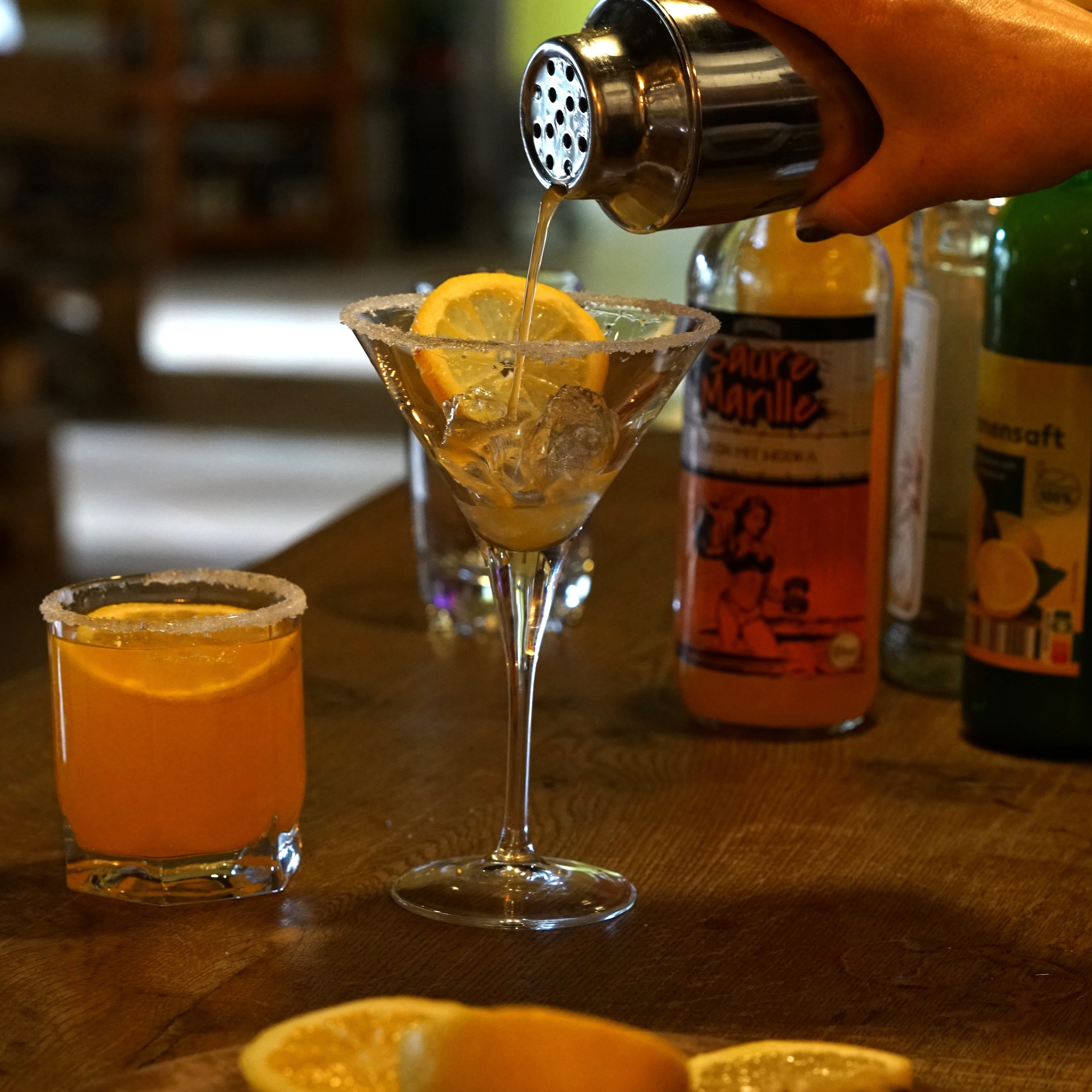 Das Bild zeigt eine Coctail Bar mit zwei orange farbenen Cocktails aus suaren Marille Likör